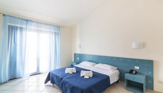 Camera moderna con letto matrimoniale, copriletto blu e tende azzurre.