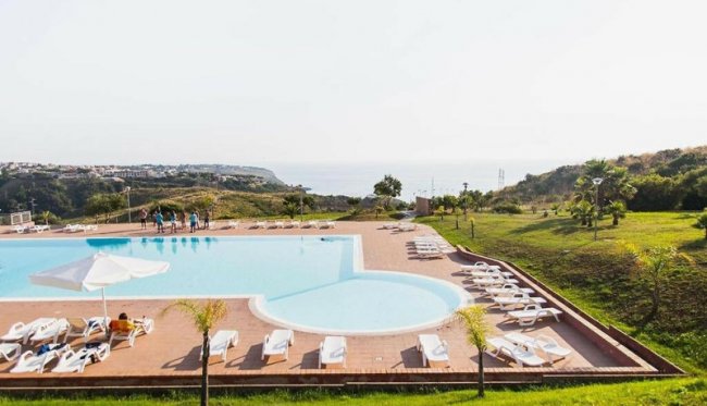 Piscina esterna con lettini, prato curato e vista panoramica.