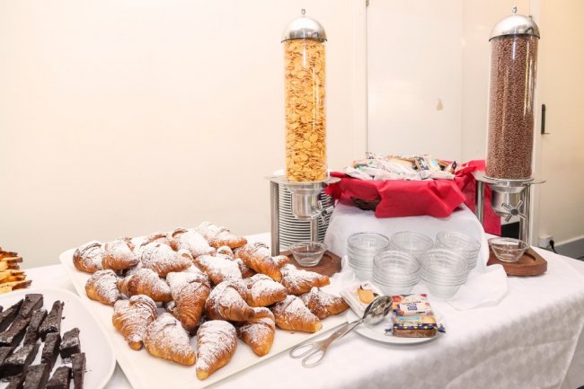Buffet di colazione con croissant, cereali in dispenser e piatti di dolci.