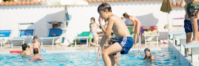 Ragazzo in aria mentre salta in piscina affollata.