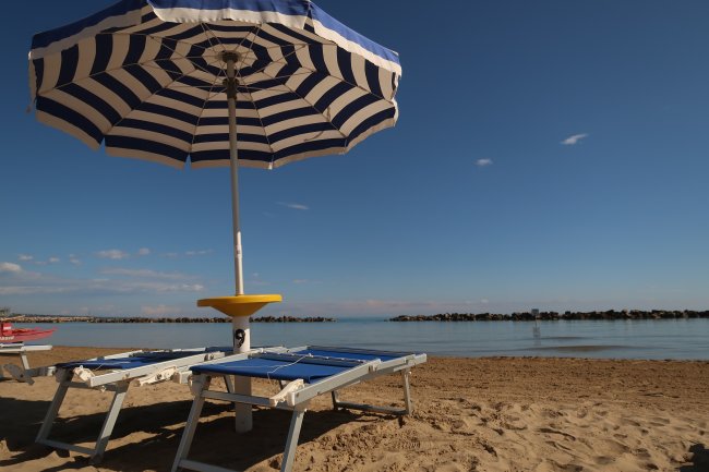 Ombrellone blu e bianco su spiaggia vuota.