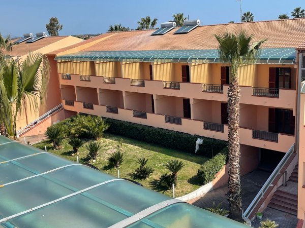 Edificio rosa a più piani con balconi e palme davanti, visibile in una giornata soleggiata.