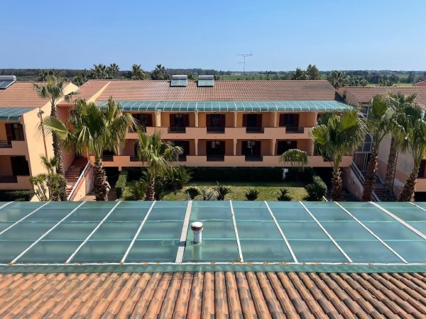 Vista di un edificio rosa a due piani con balconi, circondato da palme e tetti in vetro verde.