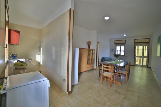 Interno di soggiorno con tavolo e cucina in fondo.