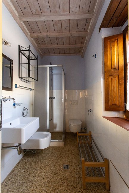 Bagno con doccia, lavabo, wc e finestra in legno.