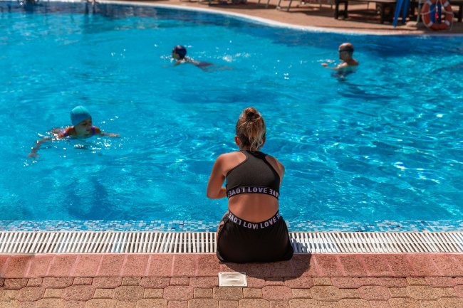 Persona seduta accanto a una piscina con persone che nuotano.