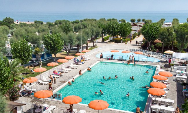 Piscina affollata con ombrelloni arancioni e vista sul mare.