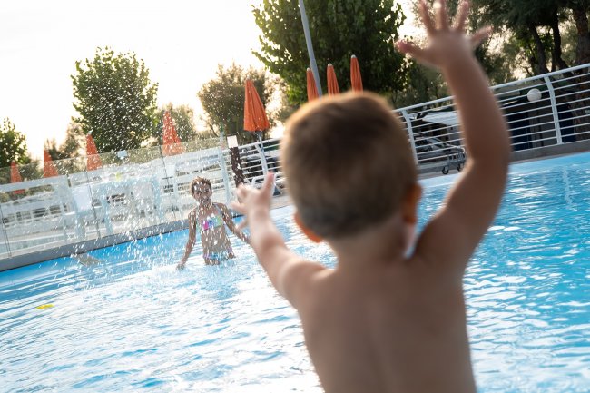 Bambino gioca in piscina spruzzando acqua con amico.