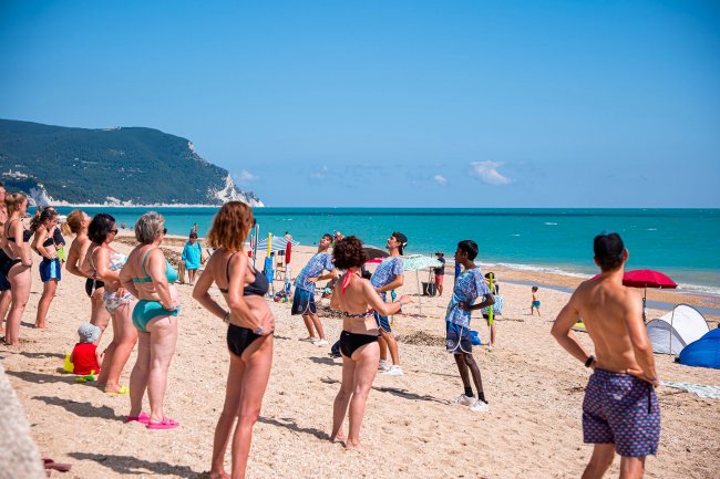 Persone fanno ginnastica sulla spiaggia, in costume da bagno.