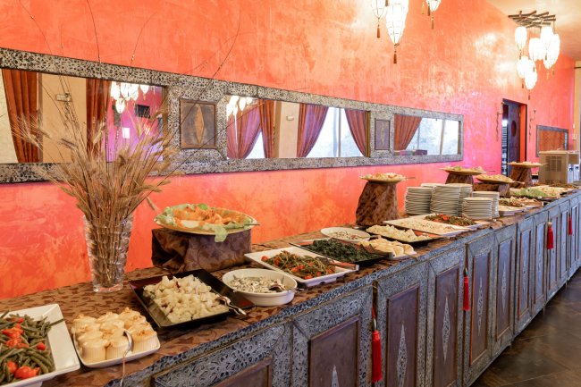 Un buffet con piatti diversi su un tavolo ornato, pareti arancioni e specchi decorativi.