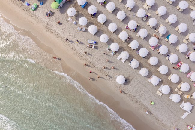 Ombrelloni bianchi allineati su una spiaggia con bagnanti e onde che lambiscono la riva.