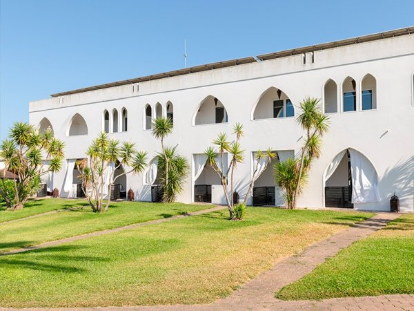 Edificio bianco con archi e palme su prato verde.