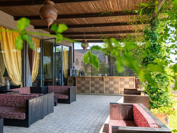 Terrazza coperta con sedute, tende gialle e lampade sospese.