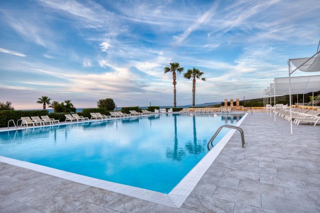 Piscina esterna con lettini e palme sotto un cielo blu.