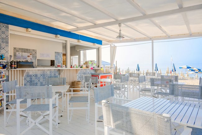 Bar sulla spiaggia con tavoli bianchi e sedie grigie.