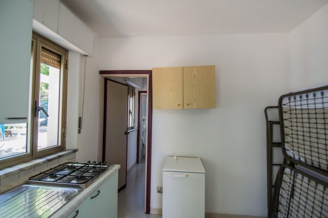 Cucina con fornello, finestra e piccolo frigo bianco.