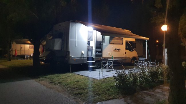 Camper illuminato di notte con tavolo fuori.