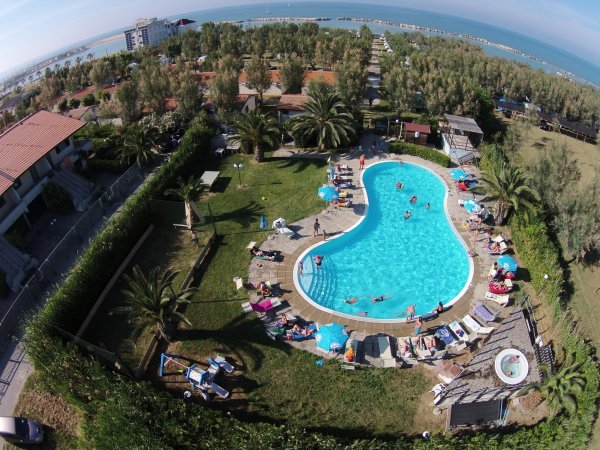 Piscina a forma libera con lettini e persone. Vista mare sullo sfondo.