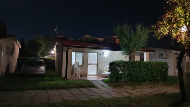 Casa piccola illuminata di notte con auto parcheggiata accanto.