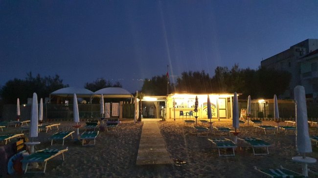 Stabilimento balneare illuminato di sera con lettini sulla sabbia.