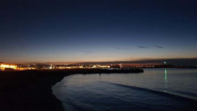 Spiaggia illuminata al crepuscolo con vista su luci cittadine.
