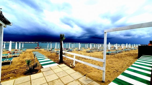 Spiaggia con ombrelloni sotto cielo nuvoloso.
