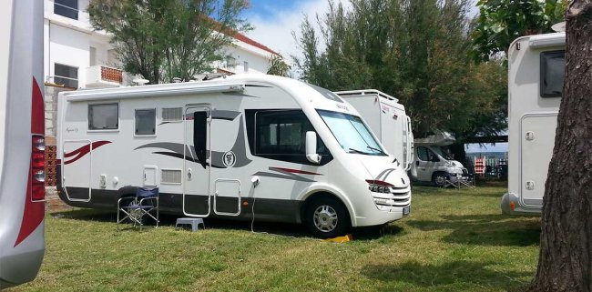 Camper bianco parcheggiato su erba con sedie pieghevoli.