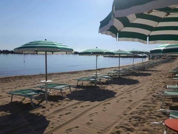 Spiaggia con ombrelloni e lettini verdi fronte mare.