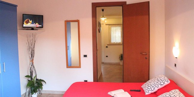Camera con letto rosso, TV e armadio blu.