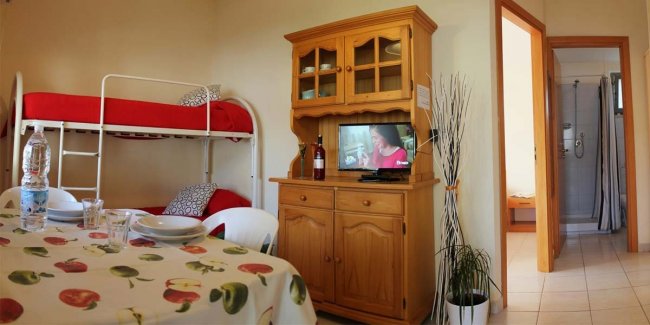 Interno con tavolo, letto a castello rosso e TV accesa.