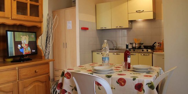 Cucina con tavolo apparecchiato e televisore acceso.