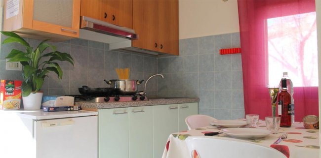 Cucina con piante, stoviglie e finestra con tenda rosa.