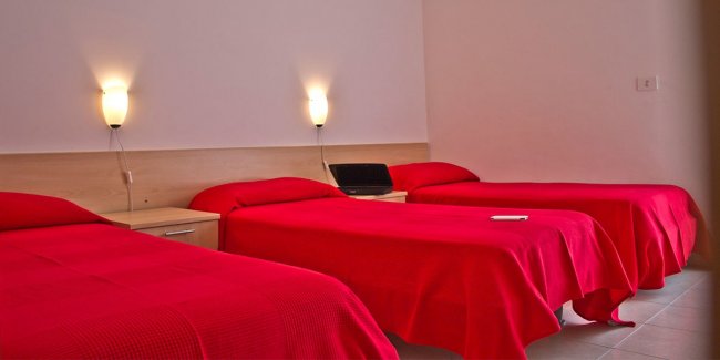 Tre letti singoli con coperte rosse e luci da parete.
