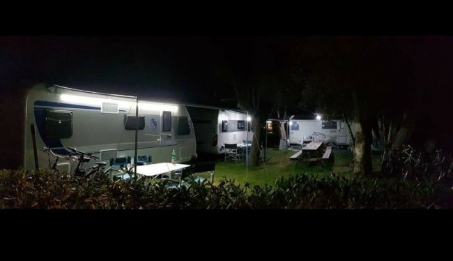 Campeggio notturno con roulotte illuminate.