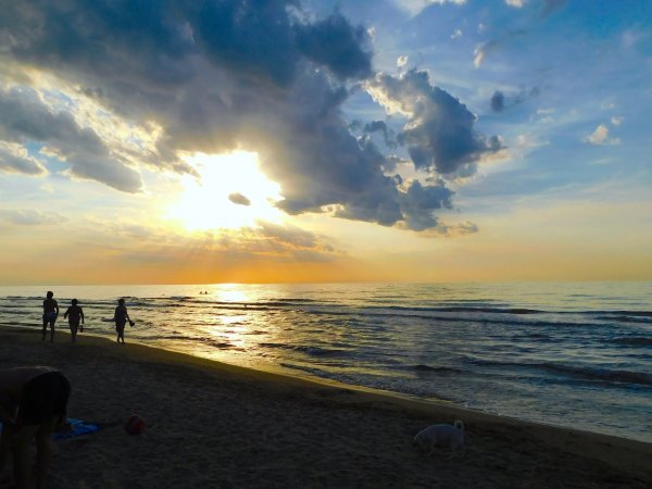 Spiaggia al tramonto con persone che camminano sulla sabbia.