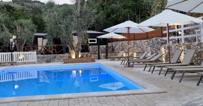 Piscina al tramonto con alberi di ulivo e sdraio.