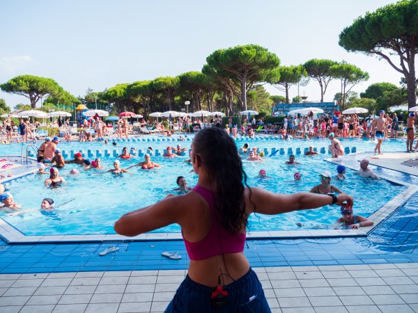 Persona insegna aerobica a bordo piscina affollata.