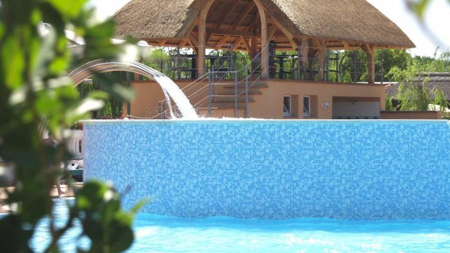Una cascata in piscina sotto una tettoia di paglia.