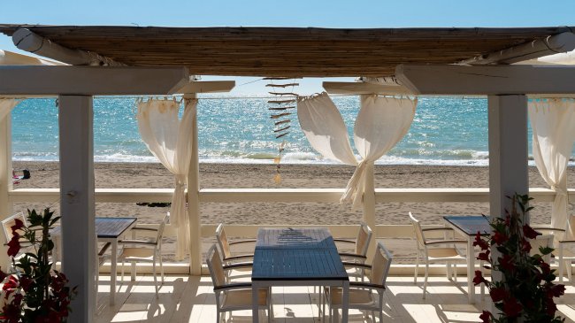 Tavoli e sedie sotto una pergola sulla spiaggia.