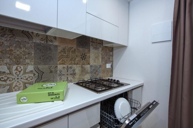 Cucina con piano cottura, lavastoviglie aperta e decorazioni in maiolica.