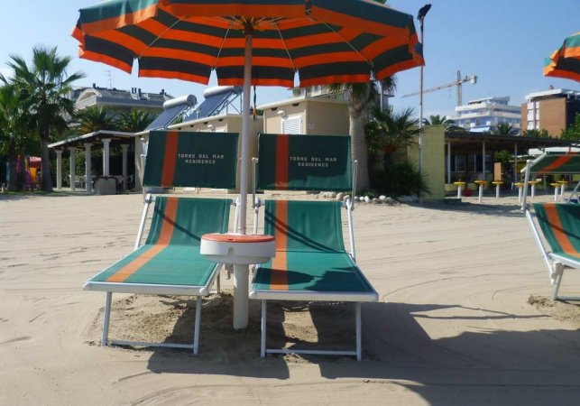 Due lettini con ombrellone su sabbia.