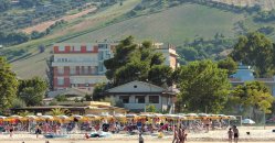 Lido affollato con ombrelloni e colline verdi sullo sfondo.