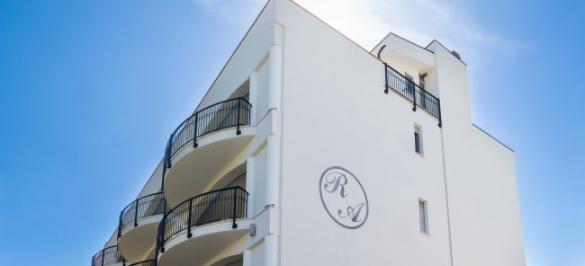 Edificio bianco con balconi curvi e sole.