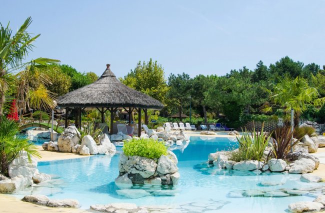 Piscina con gazebo di paglia e sedie a sdraio tra piante tropicali.
