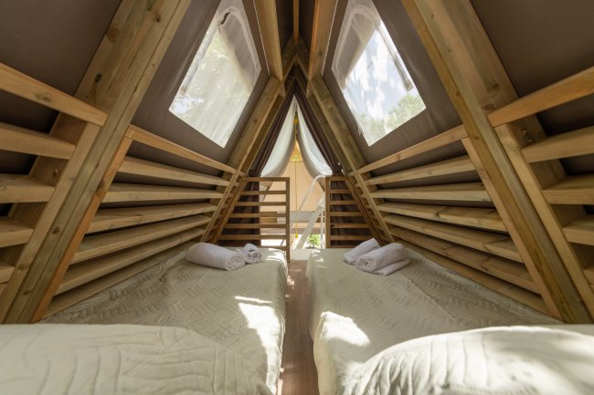 Interno di una tenda A-frame con due letti e asciugamani.