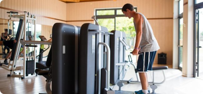 Uomo utilizza attrezzi in una palestra luminosa.