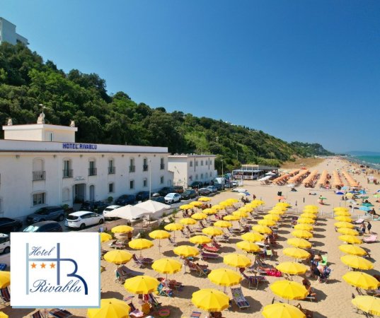 Spiaggia con ombrelloni gialli di fronte a hotel bianco.