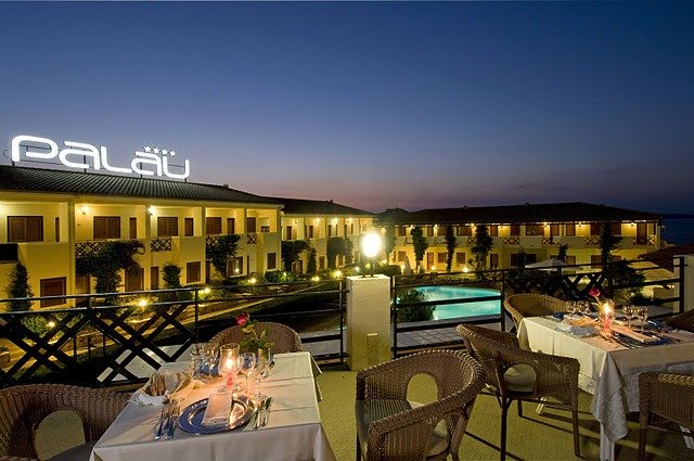 Ristorante all'aperto di sera con tavoli apparecchiati e vista su piscina illuminata.