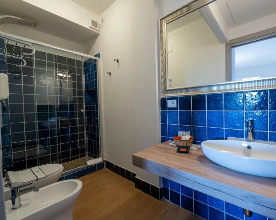 Bagno moderno con piastrelle blu, lavabo su piano in legno e doccia con pareti in vetro.
