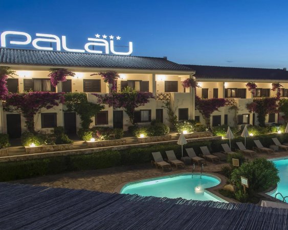 Edificio alberghiero con piscina illuminata di sera; scritta Palau sopra il tetto.